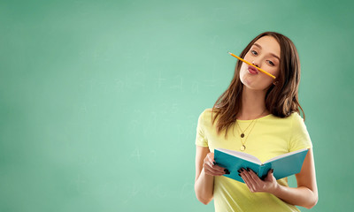 education, school and people concept - teenage student girl in yellow t-shirt with diary or notebook and pencil-mustache over green chalk board background