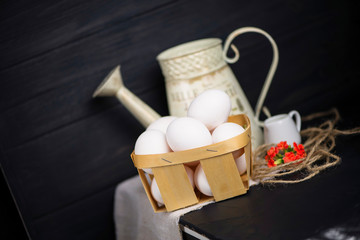 set of white raw eggs in a basket and a jug on a dark background