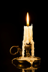 Lit candle in a candlestick on a black background