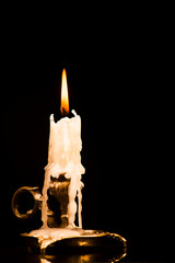 Lit candle in a candlestick on a black background