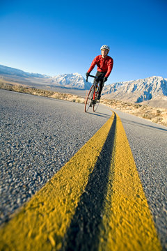 A female cyclist riding uphill above the Owen's Valley with the snowy Sierra Nevada in the background.