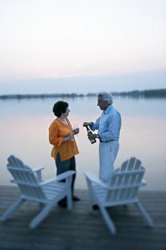 A couple in their 50's open a bottle of champagne and celebrate life on a boat dock overlooking the Chesapeake Bay at sunset near St. Michael's, Maryland.  (releasecode: CM_MR1004, MR_MR1005)