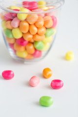 food, confectionery and sweets concept - close up of glass jar with colorful candy drops over white background