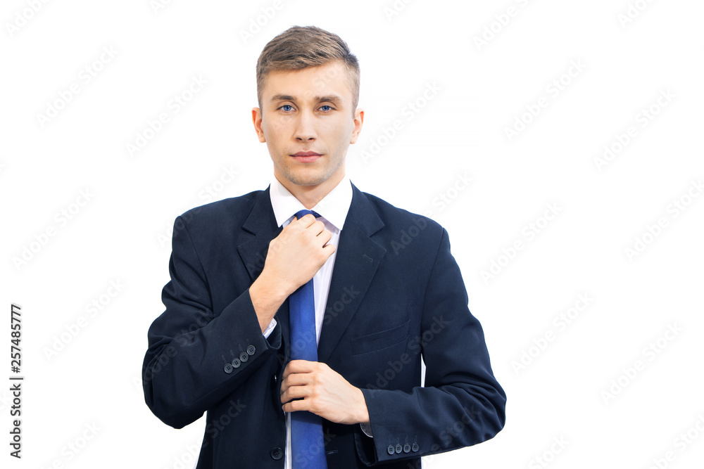 Wall mural young attractive serious business man straightens bright blue tie, isolated on white