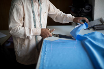A tailor cuts blue cloth with scissors.