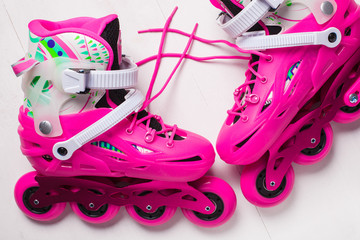 A pair of pink stylish roller skates on a white wooden background