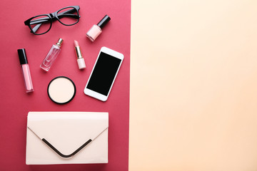 Handbag with cosmetics, smartphone and glasses on colorful background