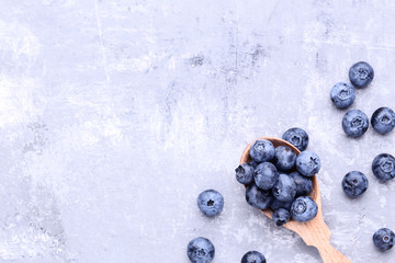 Ripe blueberries with spoon on grey background