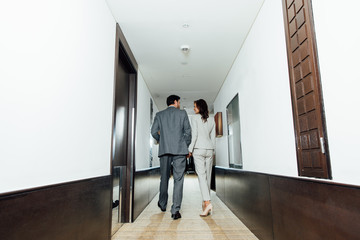 confident businessman businesswoman in formal wear holding hands and walking in hotel corridor