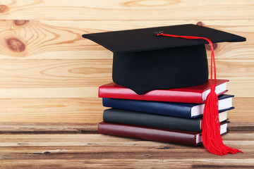 Graduation cap with stack of books on brown wooden table