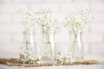 White gypsophila flowers in glass bottles on brick wall background