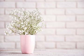 White gypsophila flowers in pink cup on brick wall background
