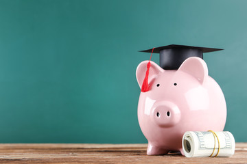 Piggybank with graduation cap and dollar banknotes on brown wooden table