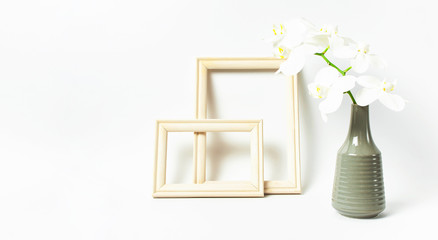 White Phalaenopsis orchid flowers in gray vase and wooden photo frames on white background. Tropical flower, branch of orchid. Holiday, Women's Day, Flower Card flat lay. Interior details Mockup