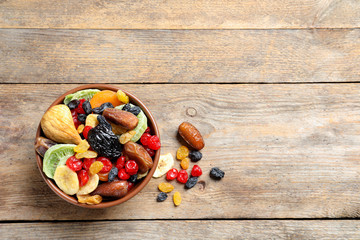 Bowl of different dried fruits on wooden background, top view with space for text. Healthy lifestyle