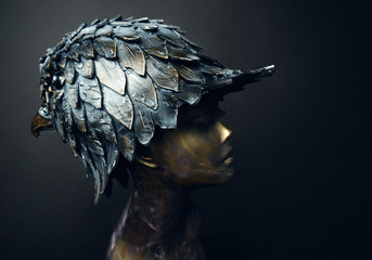 Closeup of bronze head of mannequin in decorated bronze head-wear bird head shaped, dark studio background