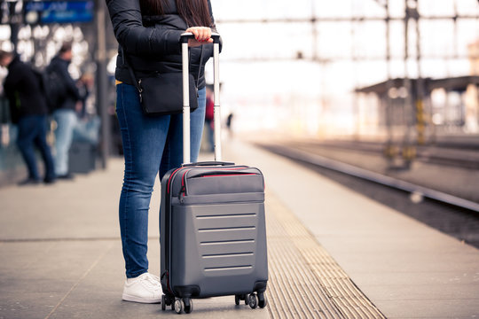 Pretty young woman with smal hand luggage waiting at the traint station for her train, transportation concept