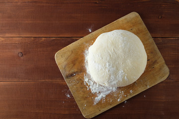 Classic wooden rolling pin with freshly prepared dough and dusting of flour on wooden background