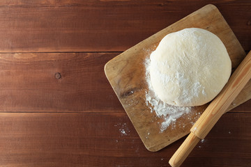 Classic wooden rolling pin with freshly prepared dough and dusting of flour on wooden background