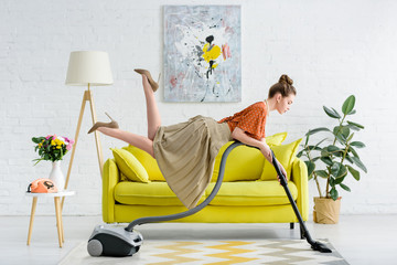 side view of elegant concentrated young woman levitating in air and vacuuming rug in living room