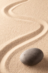curved line in the sand of a zen stone garden. A round black rock on sandy background. Concept for spirituality, harmony and balance.