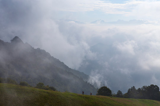 Two hikers on a mountain trail surrounded by mist and clouds. Hiking the Sentiero delle Orobie in the Italian Alps