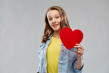 valentine's day, love and people concept - smiling pretty teenage girl in denim jacket holding red heart over grey background