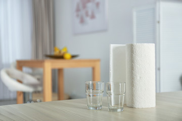 Roll of paper towels and glasses on table indoors. Space for text