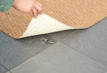 Young woman revealing hidden key under door mat, space for text