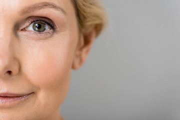 selective focus of mature woman looking at camera isolated on grey