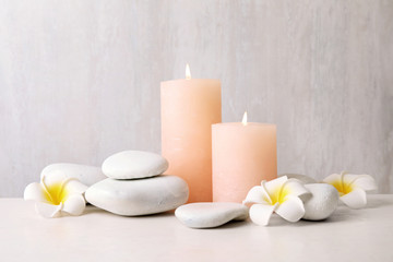 Fototapeta na wymiar Zen stones, lighted candles and exotic flowers on table against light background