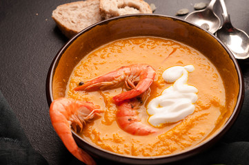 pumpkin soup with shrimps in dark bowls with silver spoons and bread on black background