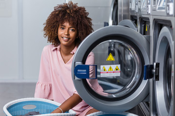 Young black African American woman washing her clothes in a automatic laundry