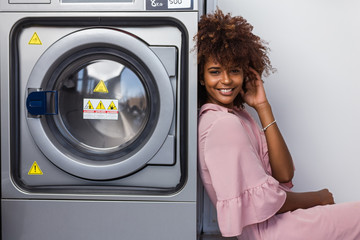 Young black African American woman waiting her clothes to be washed in a automatic laundry