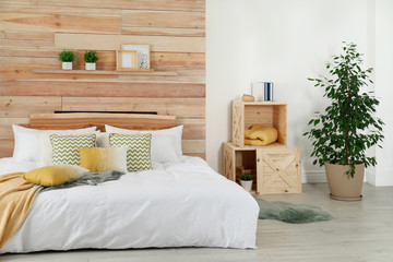 Stylish room interior with comfortable bed near wooden wall