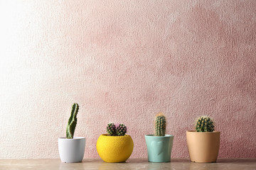 Different potted cacti on table near color background, space for text. Interior decor