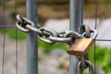 Closeup of a stainless steel chain and brass padlock securing a metal gate.