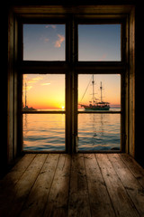 Wooden window with a table and a view of a lake with a harbor and a sailing ship. Amazing sunset, balaton, siofok hungary