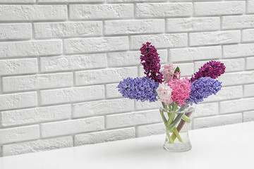 Beautiful hyacinths in glass vase on table against brick wall, space for text. Spring flowers