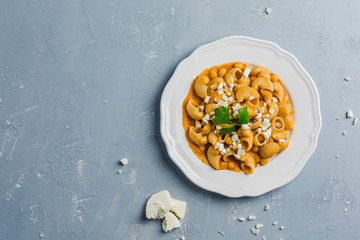 pasta Pipa the rigat with a sauce of chickpeas and tomatoes, sprinkled with feta cheese and cilantro on a white plate on a light grey background high angle