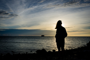 Silhouette of a girl standing alone on seashore with beautiful sky on the background at Harapan Island, Indonesia