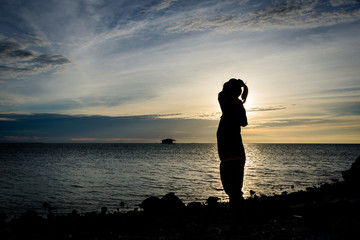 Fototapeta premium Silhouette of a girl standing alone on seashore with beautiful sky on the background at Harapan Island, Indonesia