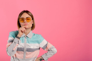 Thoughtful youbng beautiful woman look on camer and pose. She hold hand on chin. Isolated over pink...