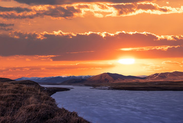 Beautiful sunset over mountains and frozen lake.