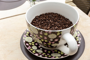 Coffee seeds in a big ceramic mug on a table background. Heap of coffee beans in cup.