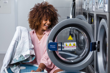 Young black African American woman washing her clothes in a automatic laundry
