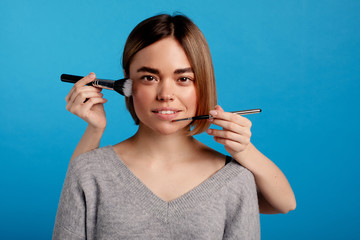 Confident nice young woman look on camera. She smile. Hands doing make up. Isolated over blue...