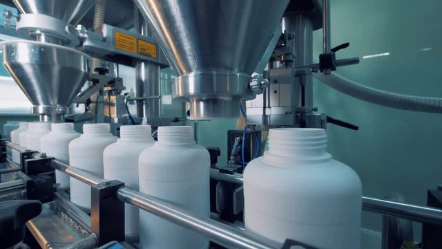 Industrial equipment is filling white plastic bottles
