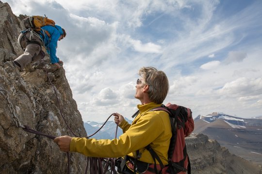 Mountaineer belays teammate on summit ridge