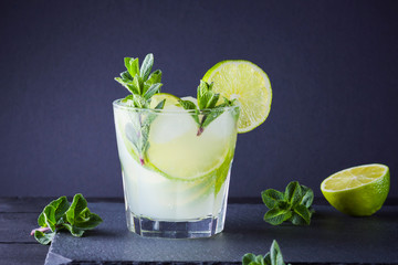 Cocktail mojito and mint on black background. Refreshing cocktail with lime and fresh mint on slate board. Summer drink with citrus and ice. Copy space